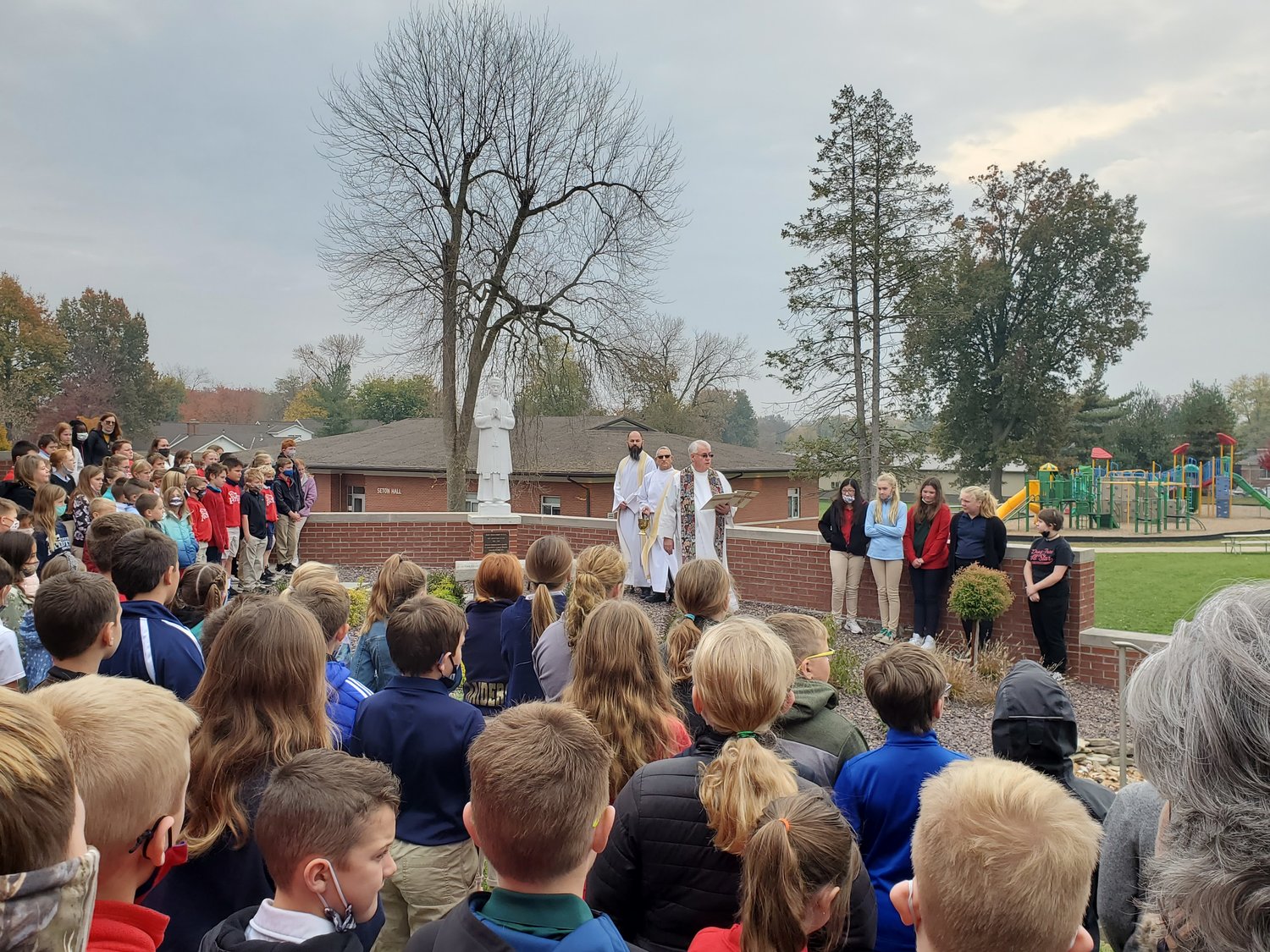 Monsignor Leo Enlow, pastor of St. Peter Parish in Quincy, Illinois, blesses the new Fr. Tolton Garden on the parish property, with students of St. Peter School watching.